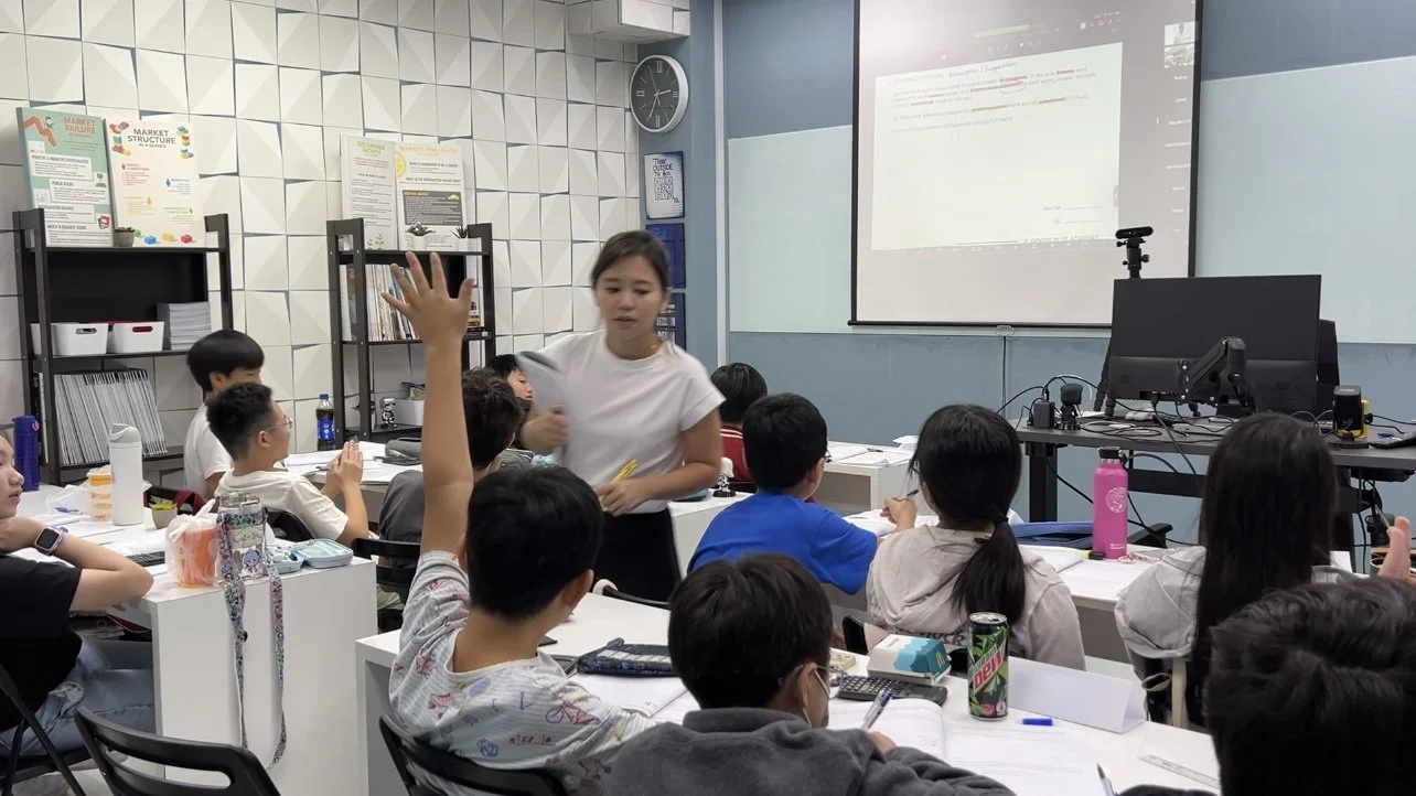 A GPA tutor teaching a small primary class, students with hands raised